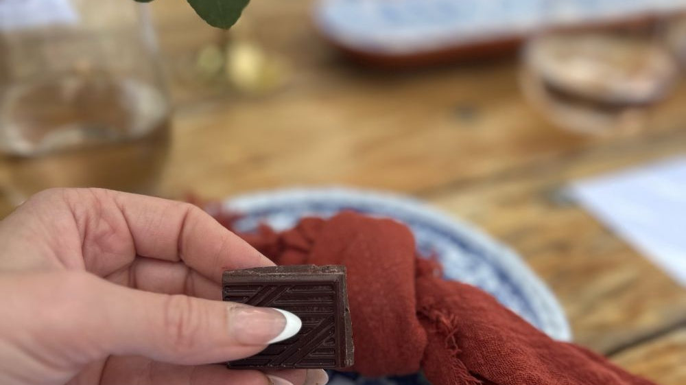 Woman holding a piece of Moksha dark chocolate, with a plate of chocolate squares in the foreground