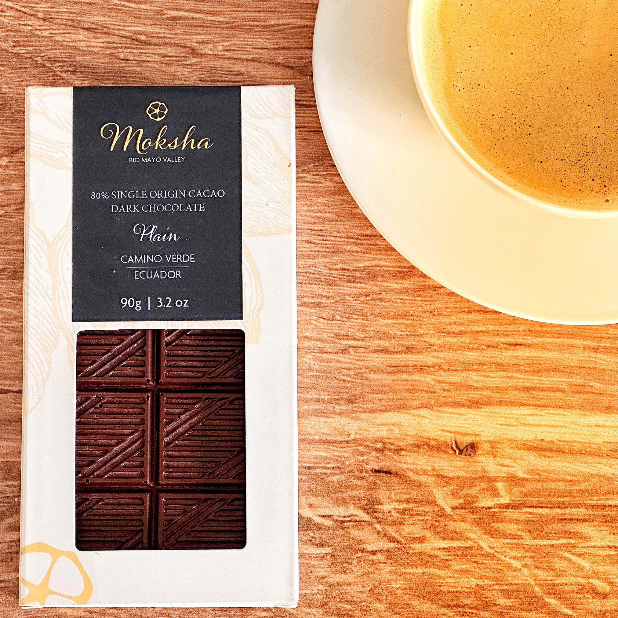 Moksha 80% chocolate bar packaging on a wooden surface with a cup of coffee.