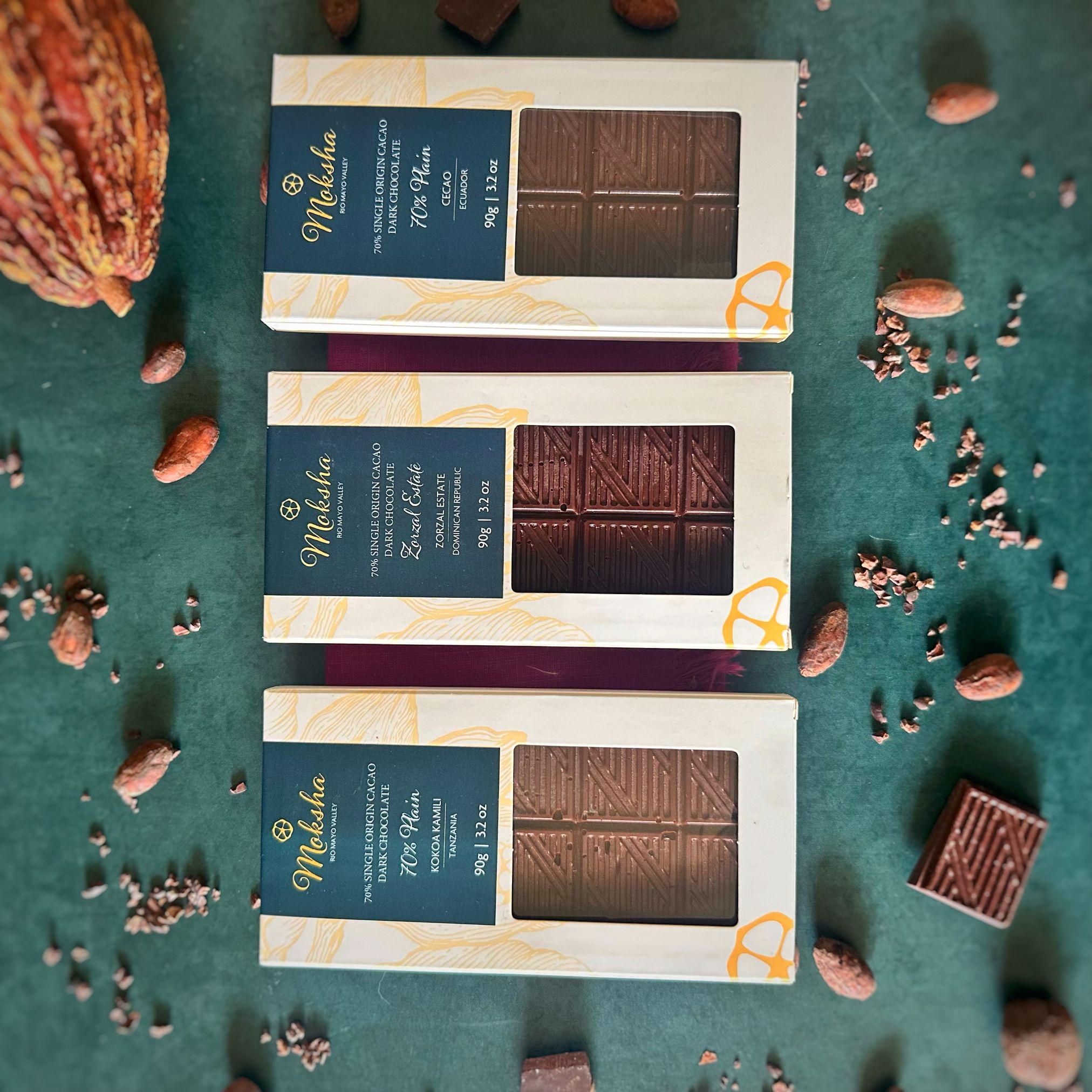 Three boxes of 70% dark chocolate bars on a green surface with cocoa beans and a cocoa pod.