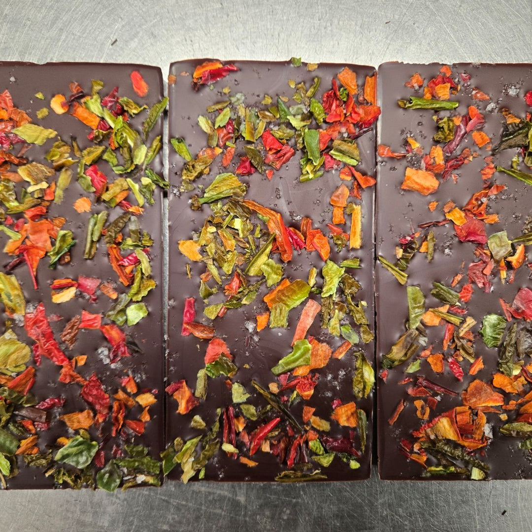 Three chocolate bars with colorful dried pueblo chile pieces on a stainless steel surface