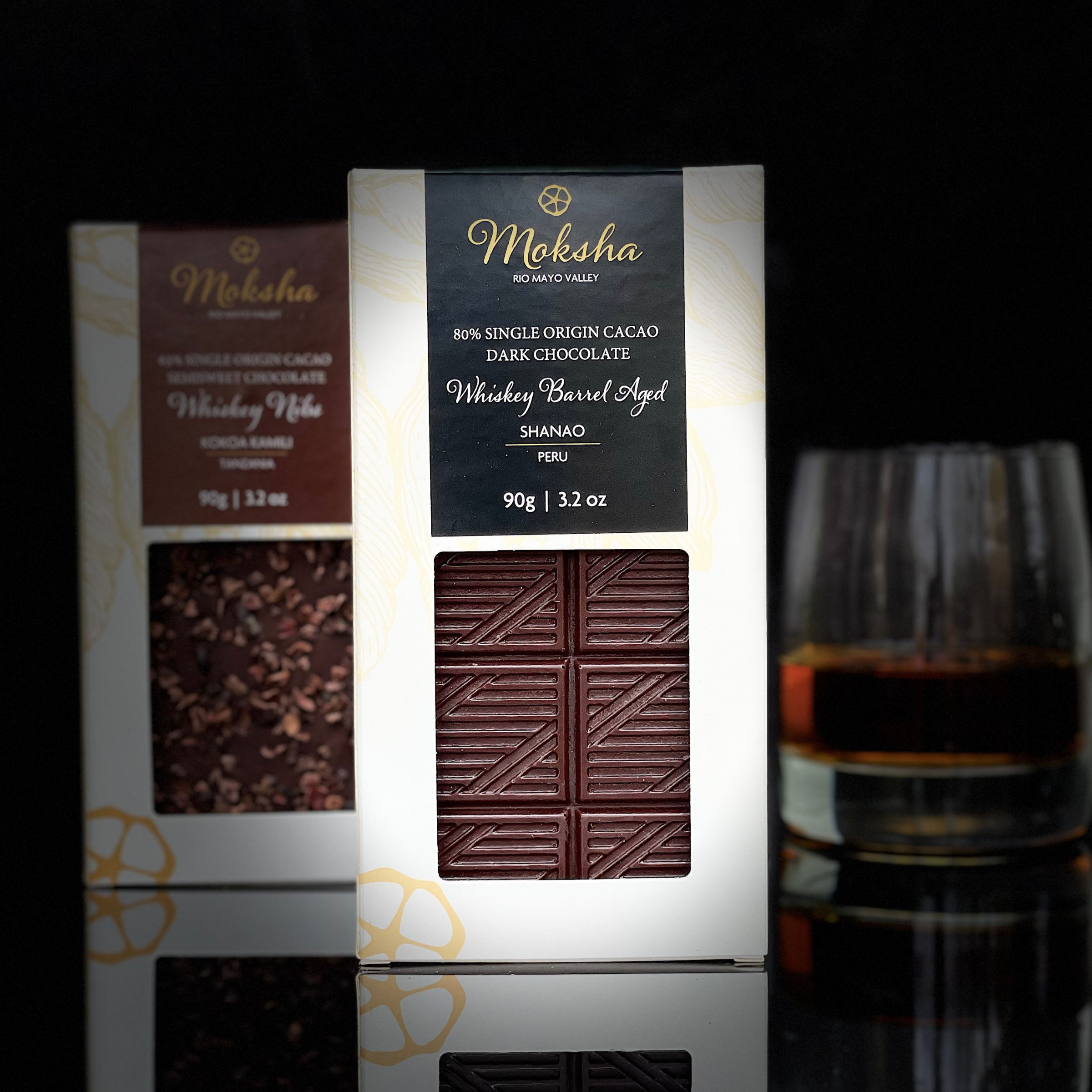 Moksha Chocolate 80% Whiskey Barrel Aged Single Origin Dark Chocolate Bar from Shanao, Peru, featuring artisan bean-to-bar vegan chocolate with a glass of whiskey on a black background."