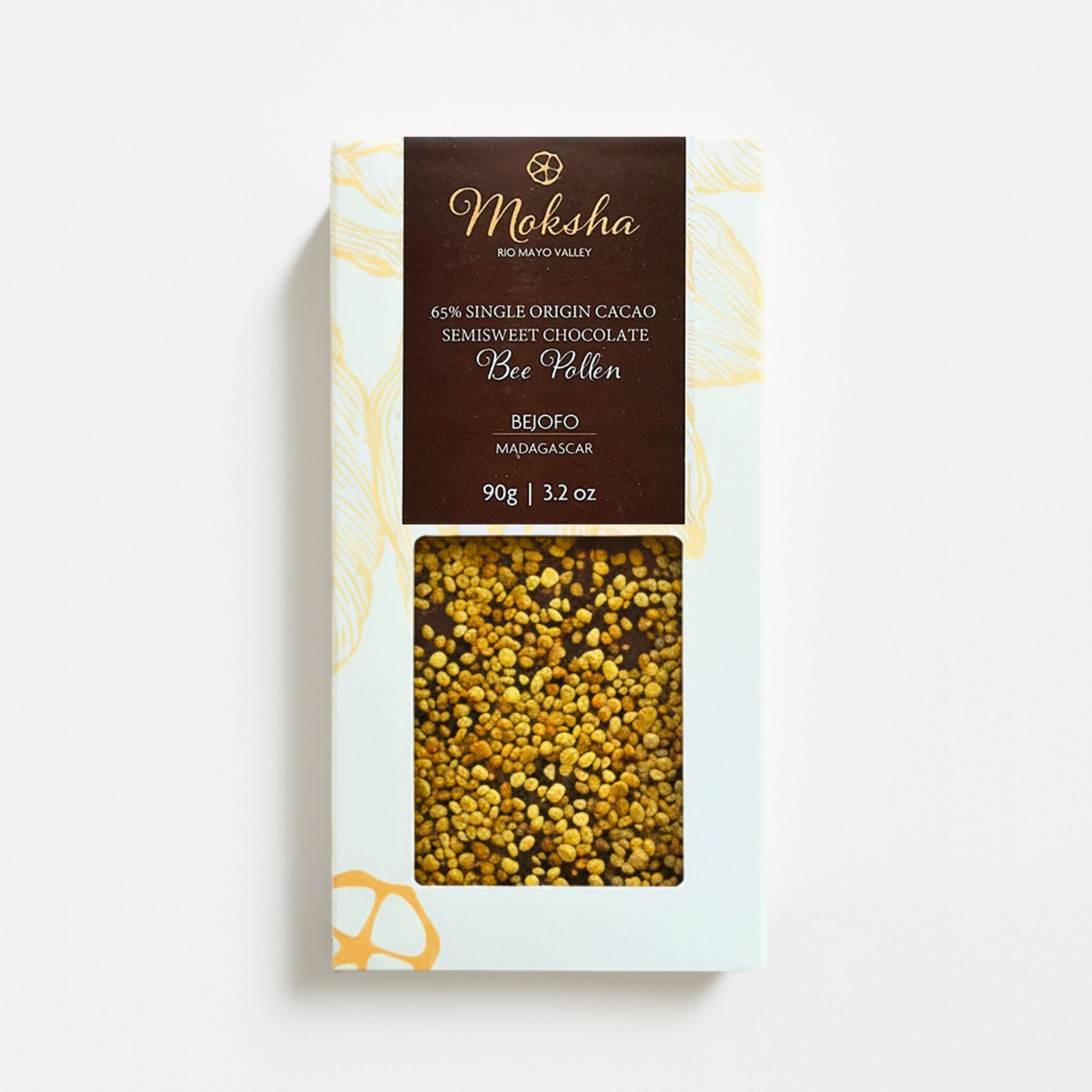 Moksha Chocolate Bee Pollen Bar in white and gold packaging with a window showing organic bee pollen on top of a 65% Madagascar chocolate bar, photographed on a clean white background.