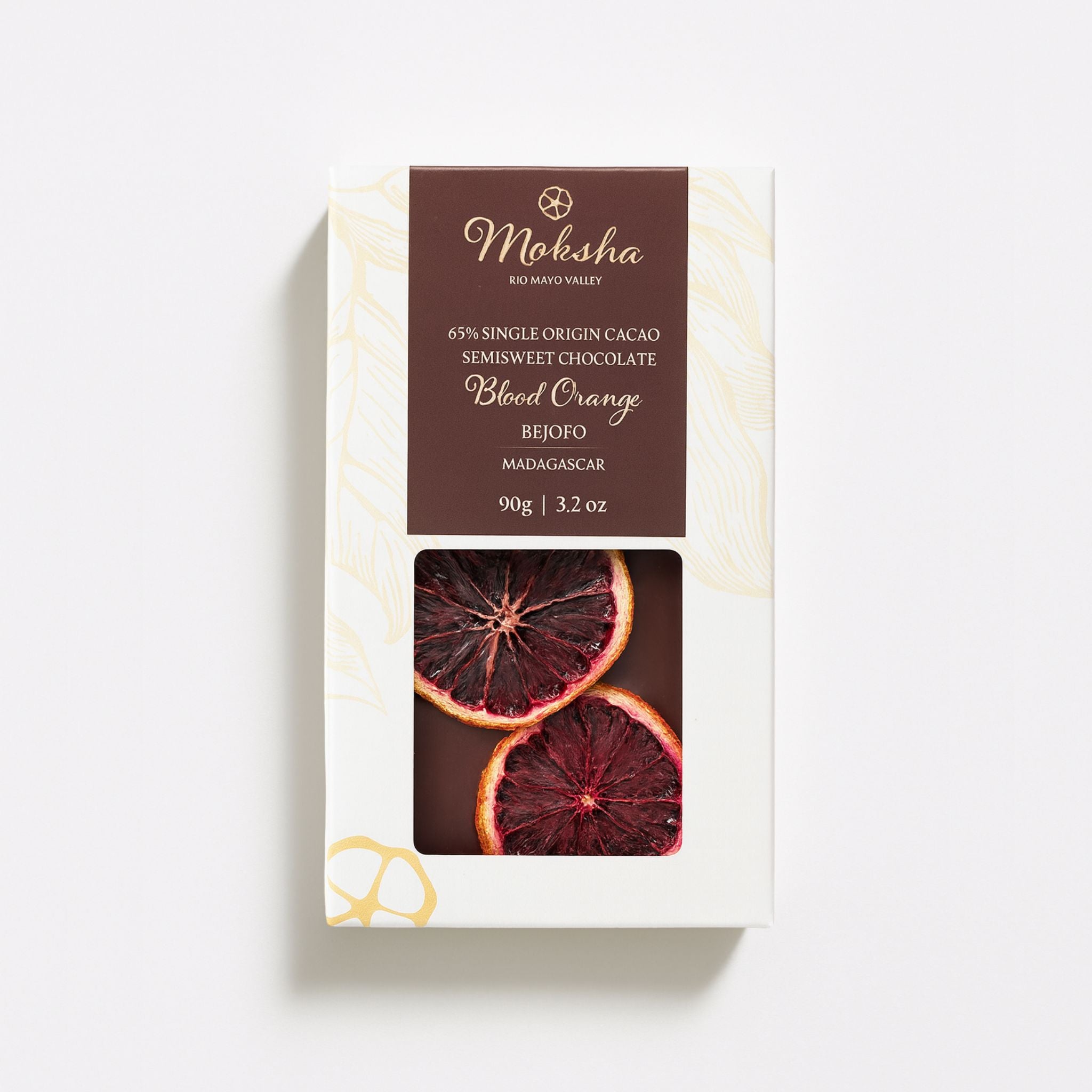 Moksha 65% Blood Orange chocolate bar in white and gold packaging with a brown label and a window showing dried blood orange slices on the chocolate surface.