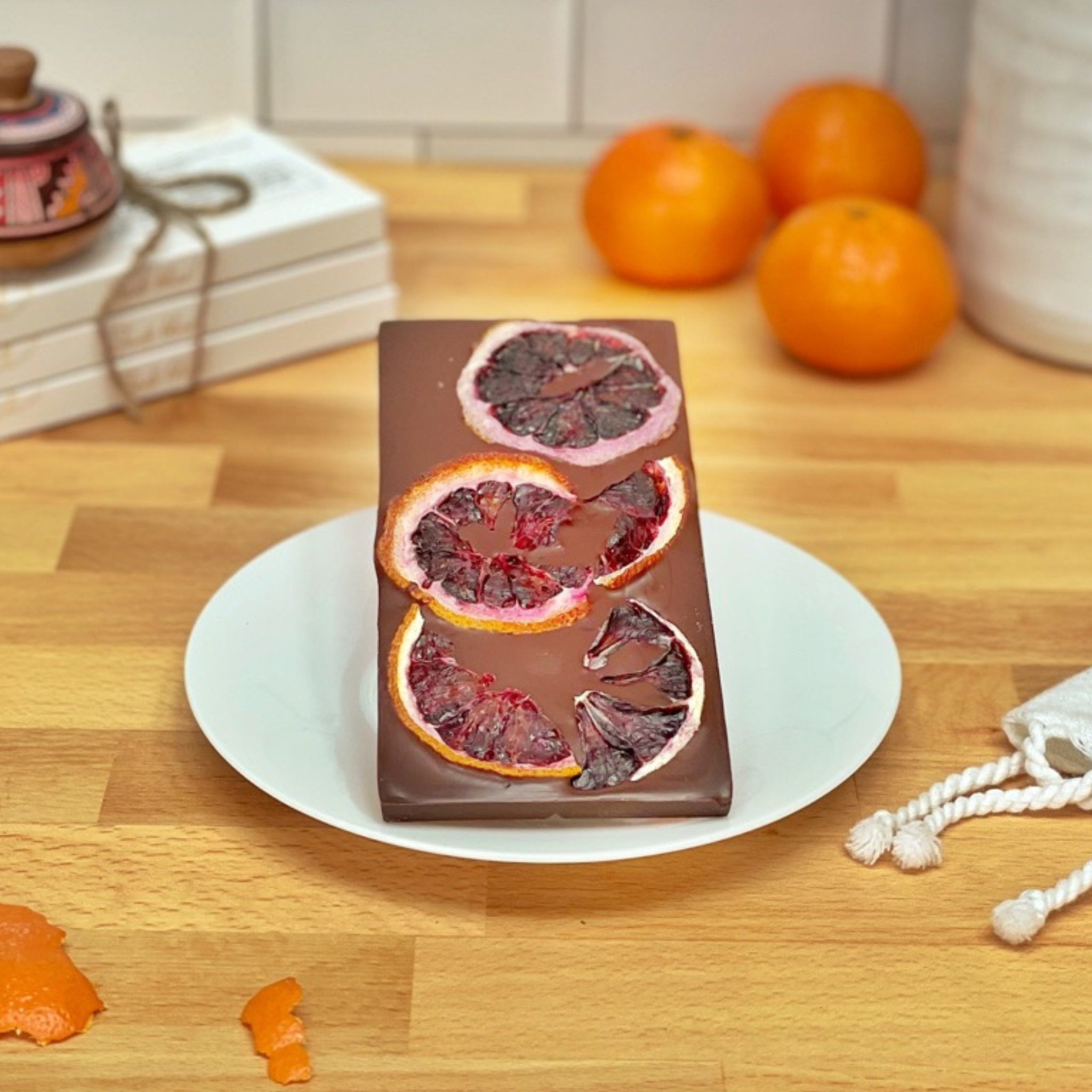 Chocolate bar with blood orange slices on a white plate on a wooden table.