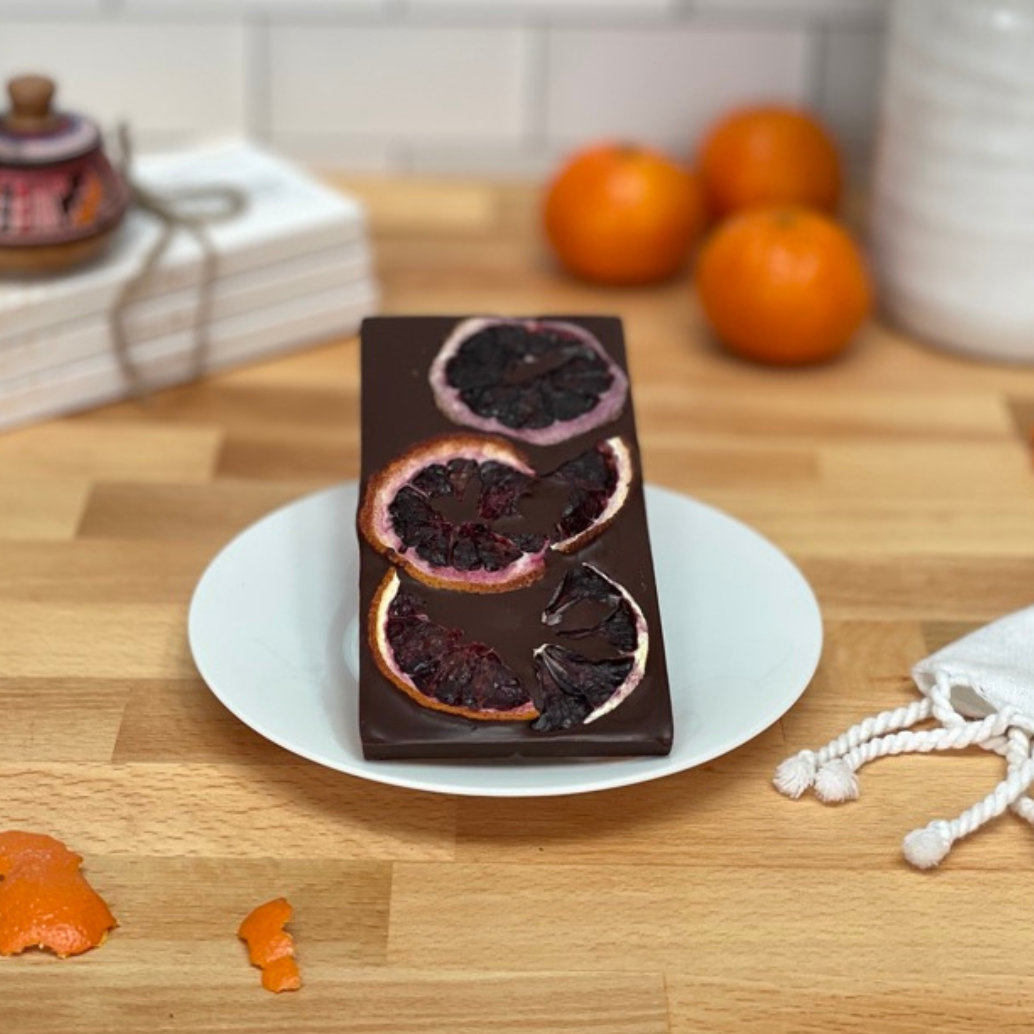 Moksha Blood Orange Chocolate bar with blood orange slices on a white plate on a wooden table.