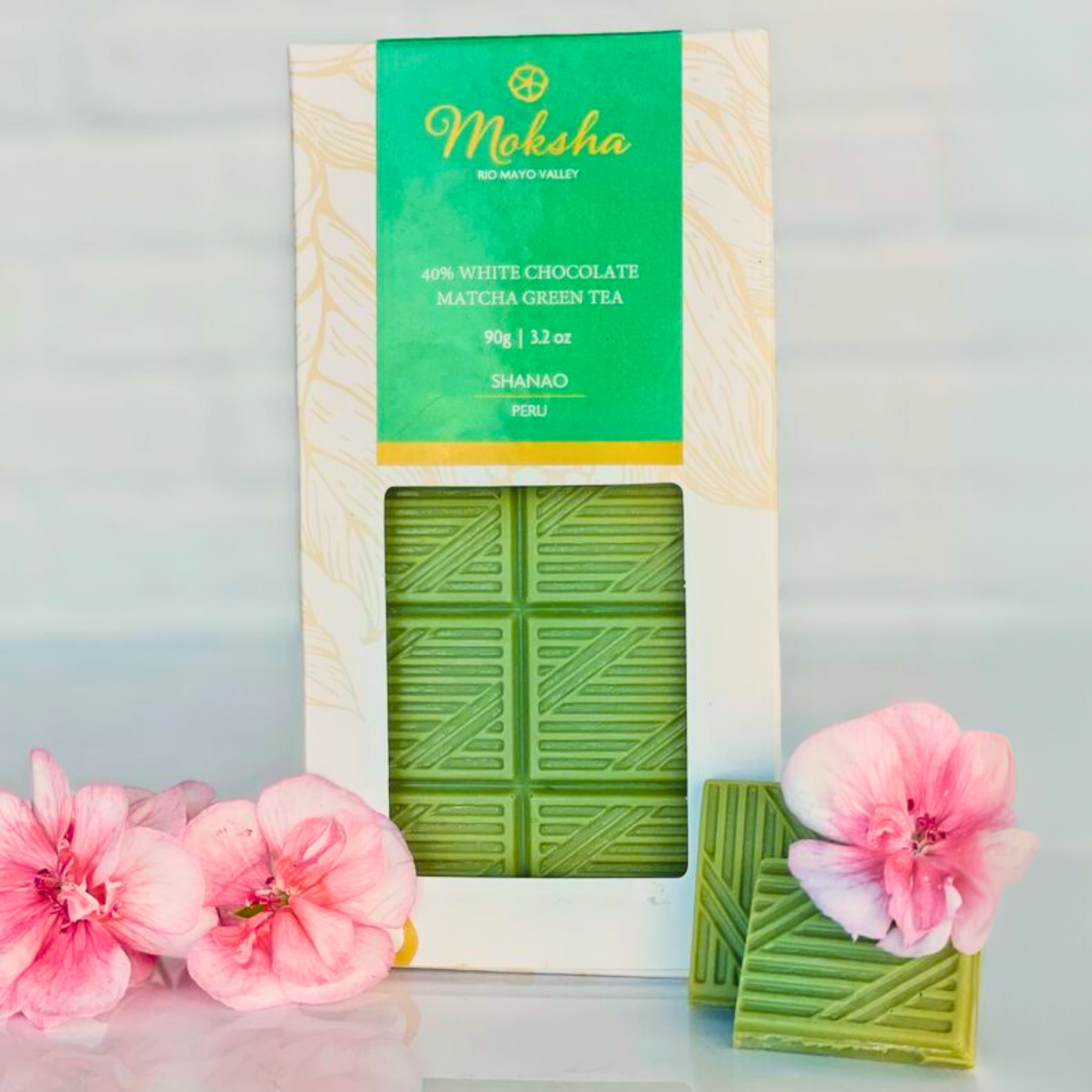 Moksha Matcha White Chocolate bar in packaging styled with pink flowers for a fresh and elegant look.