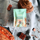Moksha Reishi Chocolate Bar with 65% dark vegan chocolate surrounded by dried reishi mushrooms and chocolate squares on a textured cloth background..