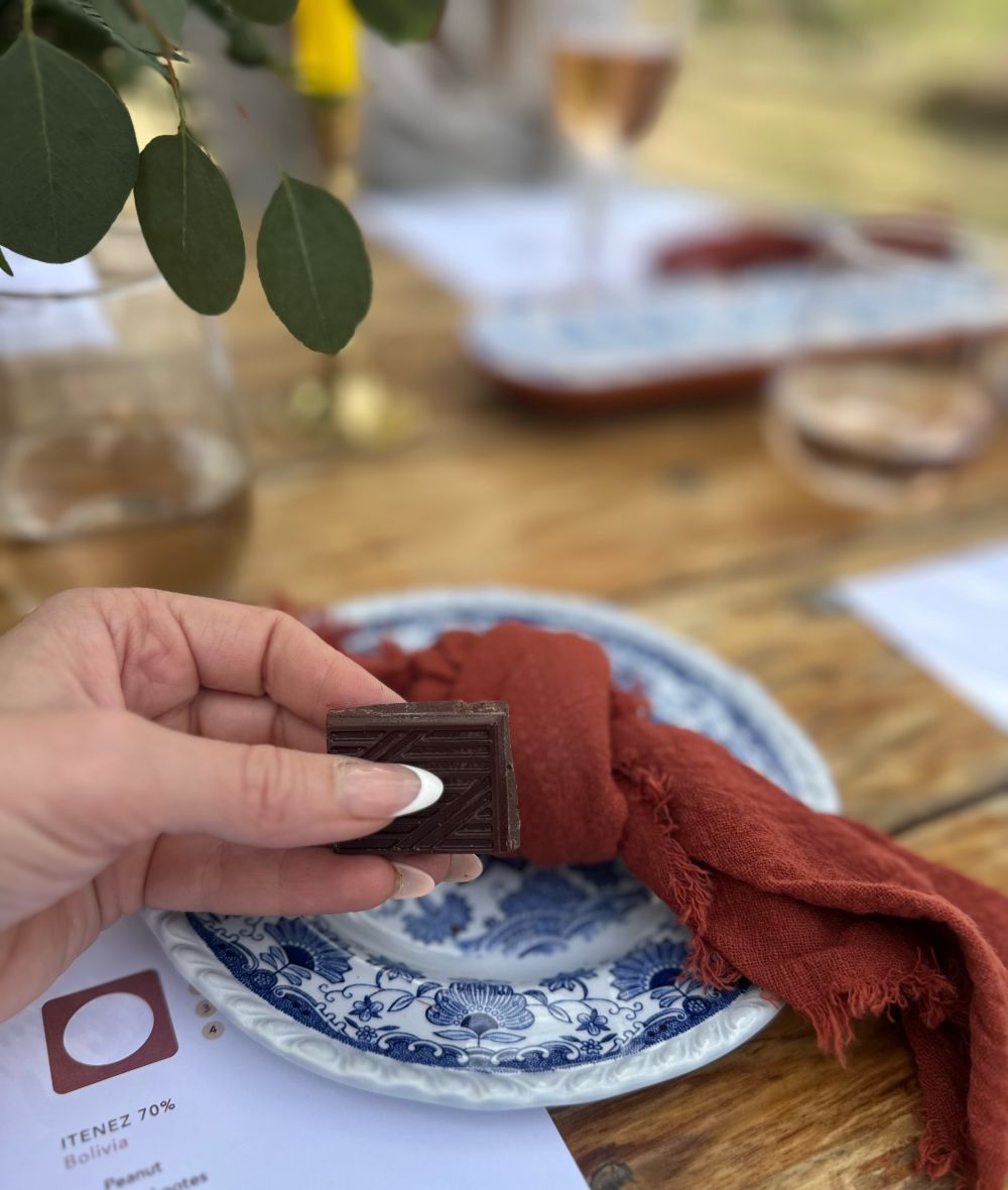 Woman holding a piece of Moksha dark chocolate, with a plate of chocolate squares in the foreground