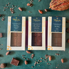Three boxes of  70% dark chocolate bars on a green surface with cocoa beans and a cocoa pod.