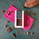 70% dark Zorzal with packaging on a pink cloth surrounded by cocoa beans and a cacao pod.