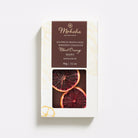 Moksha 65% Blood Orange chocolate bar in white and gold packaging with a brown label and a window showing dried blood orange slices on the chocolate surface.