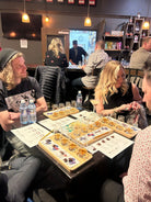 Group of people sitting around a table with board games and drinks in a casual setting.
